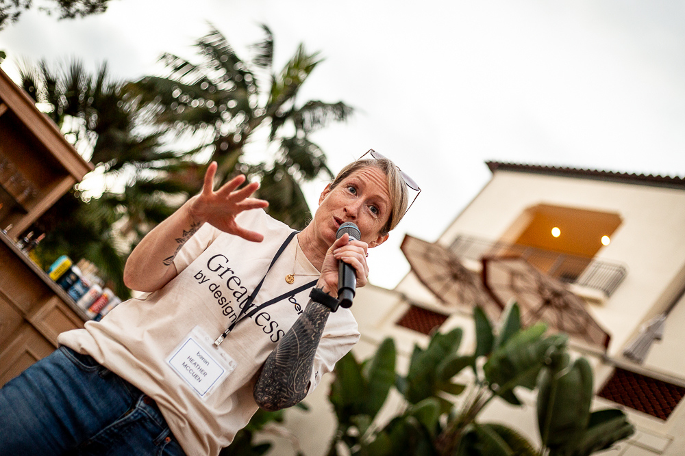 Heather McCuen speaking with a microphone in a Greatness t-shirt