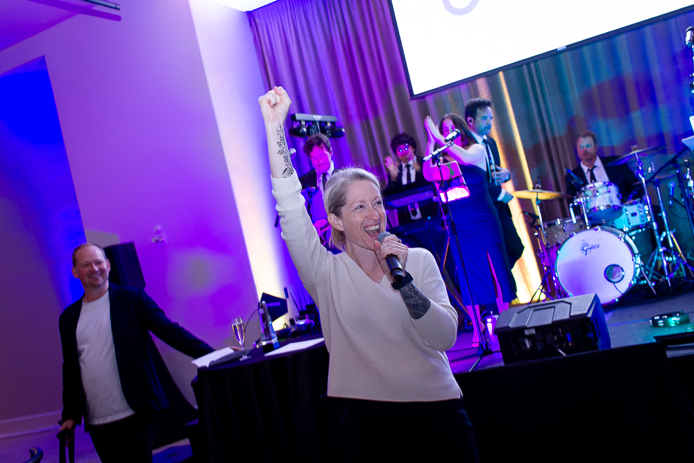 Heather McCuen on stage with her fist raised, holding a microphone