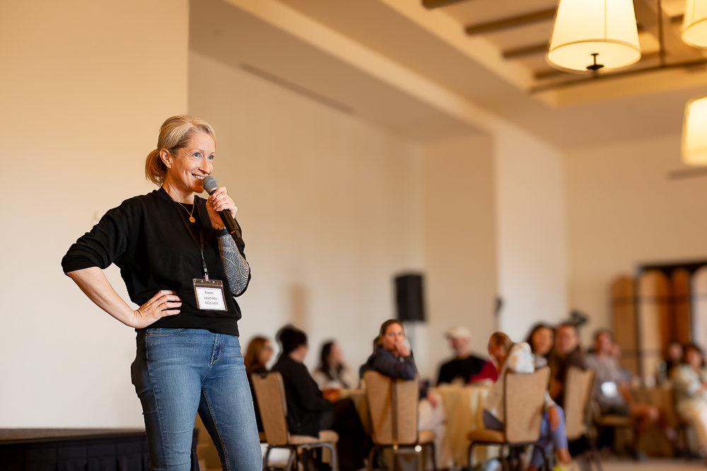 Heather McCuen speaking with a microphone at a company gathering